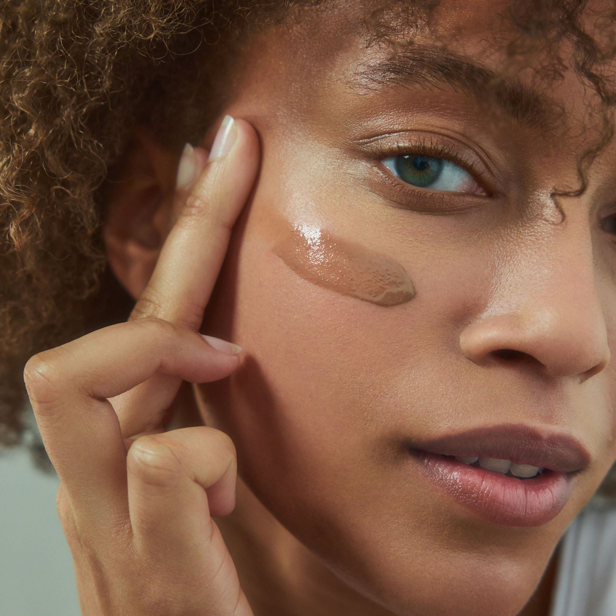 Close-up of a person applying makeup to their face with a neutral background