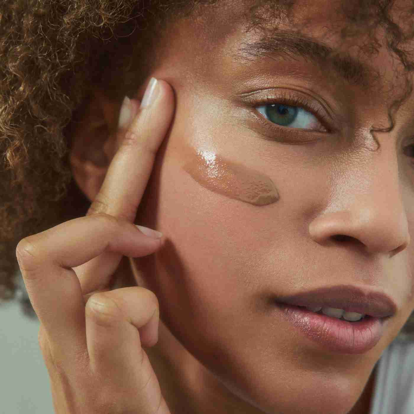 Close-up of a person applying makeup to their face with a neutral background